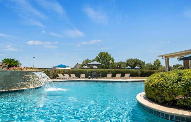 A pool with a waterfall and lounge chairs.