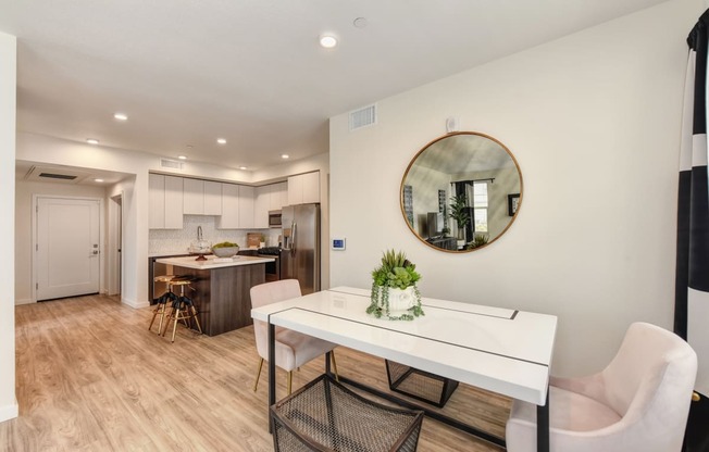 Dining area with table and chairs. Round wall mirror on dining room wall and kitchen island in the background at Morgan Ranch Apartments, Morgan Hill, California