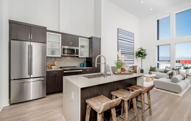 Studio Apartments for Rent Woodland Hills, CA - The Q Variel - Modern Kitchen with Custom Cabinets, Quartz Countertops, Luxury Wood Plank Style Flooring, Stainless Steel Appliances, Large Kitchen Island, High Ceilings, and Open-Concept Layout with Dining Area and Living Room Boasting Expansive Windows