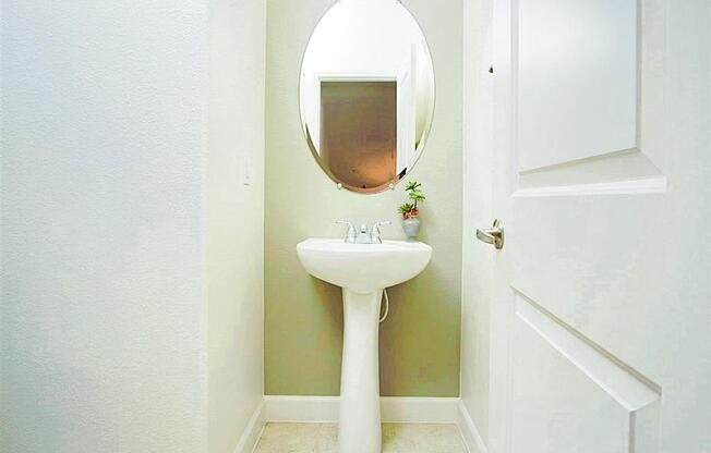 A white pedestal sink with a round mirror above it.