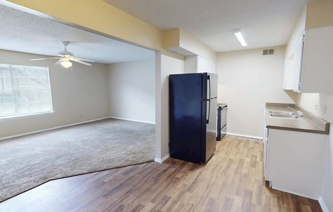A black fridge in a kitchen with wooden floors and white walls.