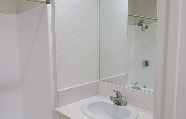 Bathroom sink with white cabinets and large mirror in one bedroom apartment at the Atrium Apartments in San Diego, CA.