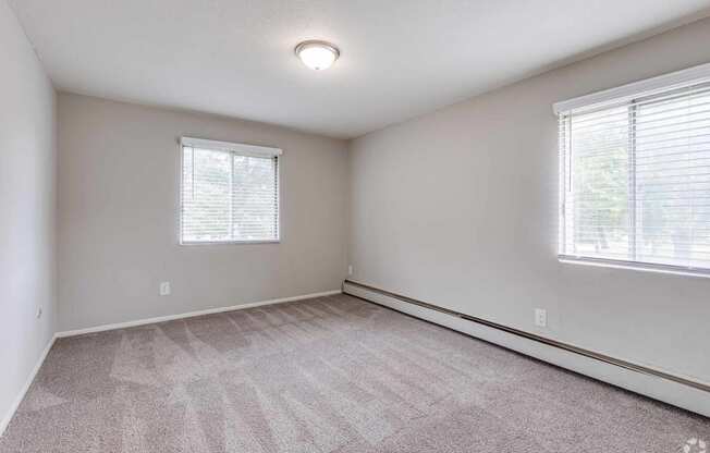 an empty living room with carpet and two windows