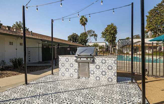 A black and white tiled outdoor kitchen area with a grill and a pool in the background.