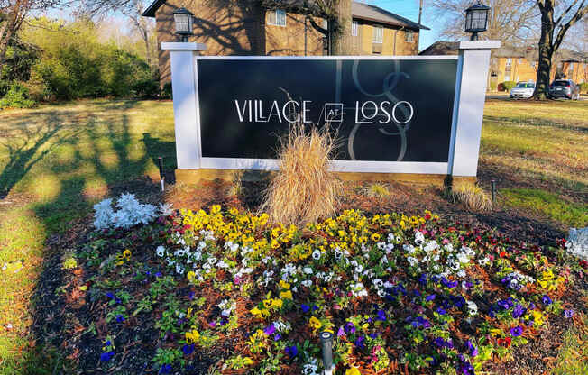 a sign for village of lasso in front of a garden of flowers