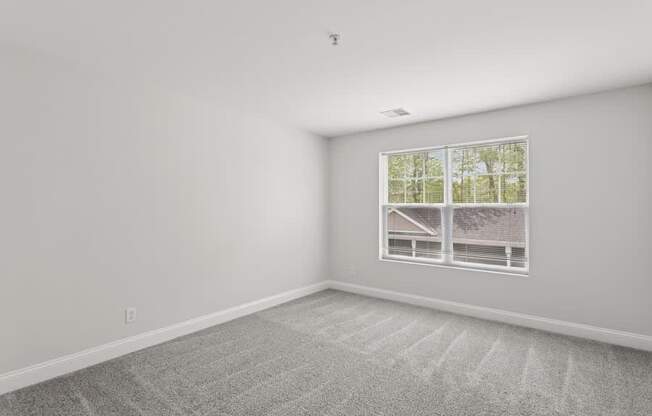 A room with a carpeted floor and a window showing a house and trees outside.