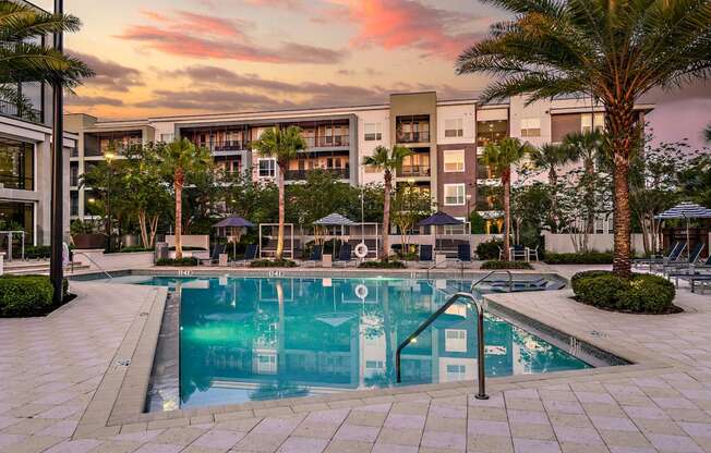 a swimming pool in front of an apartment building at sunset