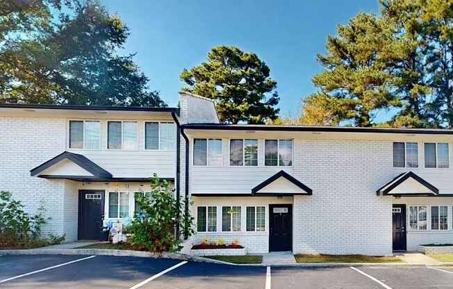 A white building with black trim and windows is surrounded by a parking lot.
