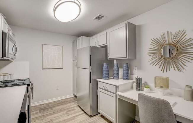 A kitchen with a refrigerator, microwave, and a desk with a chair.