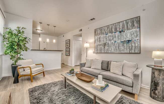 A living room with a grey couch, a wooden chair, a coffee table, and a large abstract painting on the wall.