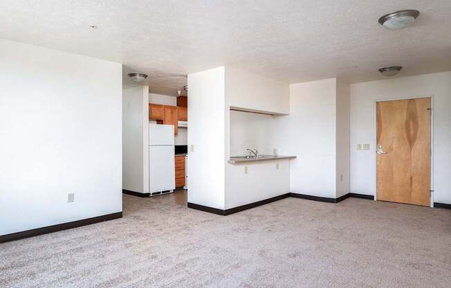 an empty living room and kitchen with a refrigerator and a sink