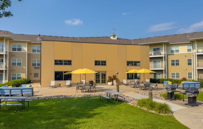 an outdoor patio with tables and umbrellas at chaska place apartments