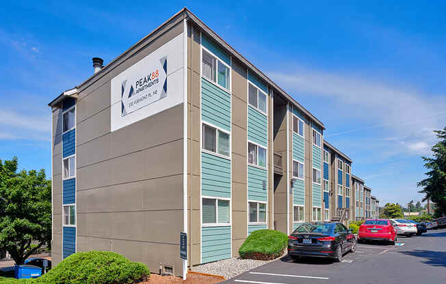 Building corner with parking below to the right. Bushes and landscaping.