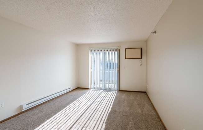 an empty living room with a sliding glass door to a balcony. Fargo, ND Eagle Run Apartments