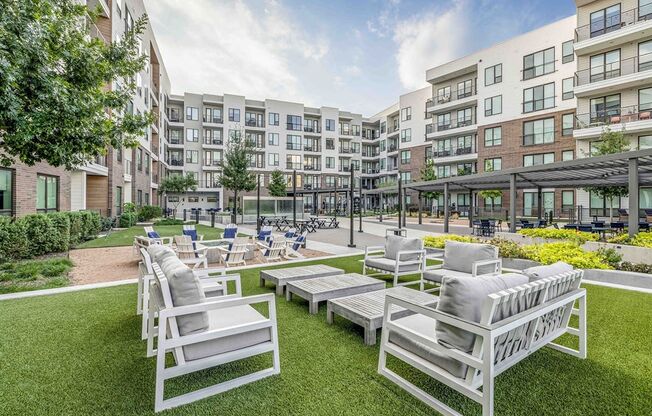 an outdoor lounge area with white chairs and lawn furniture in front of an apartment building