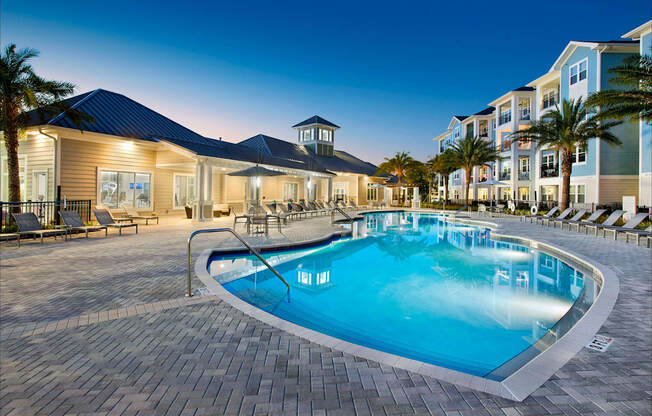 A large outdoor swimming pool surrounded by a brick patio and lounge chairs.