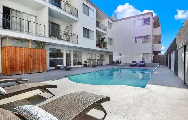 A pool surrounded by a patio with a bench and a building in the background.