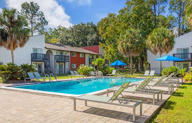A pool surrounded by lounge chairs and umbrellas with apartment buildings in the background.