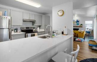 A kitchen with a white counter top and a clock on the wall.