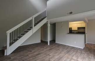 an empty living room with stairs and a kitchen