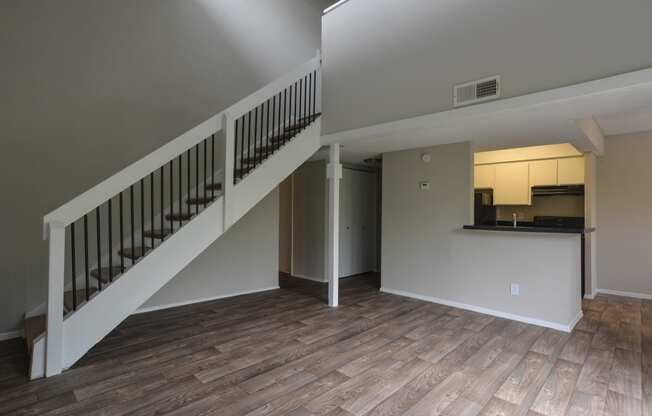 an empty living room with stairs and a kitchen