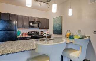 Kitchen area with sink and fridge and stove top and chairs and hanging lights and marble kitchen top