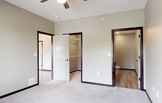 A carpeted bedroom with a ceiling fan, a walk-in closet, and an attached bathroom.