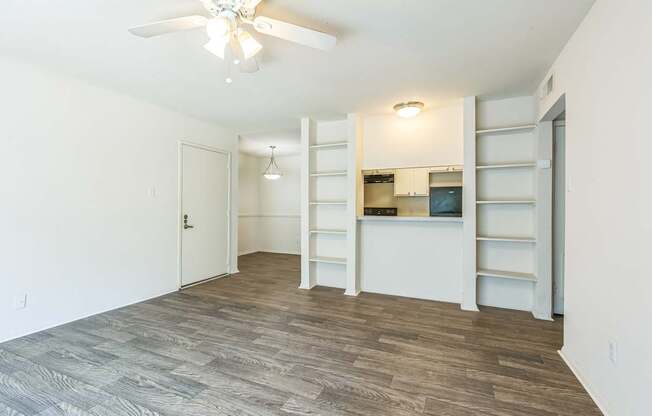 A room with a ceiling fan and a kitchenette in the background.