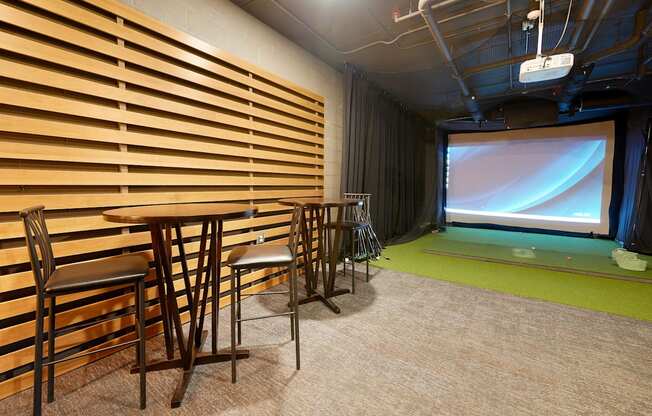 golf simulator room with chairs, artificial turf and a projector screen