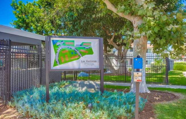 a sign in front of a park with a tree and a fence