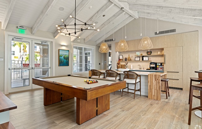 A billiard table is in the middle of a room with a kitchen area in the background.