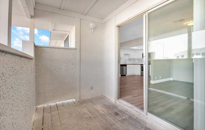 an empty room with a sliding glass door and a kitchen in the background