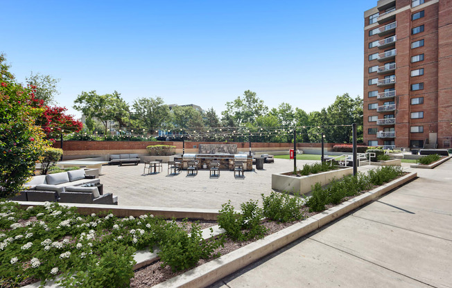 A large outdoor seating area with a concrete floor and a grassy area with a bench and a tree.