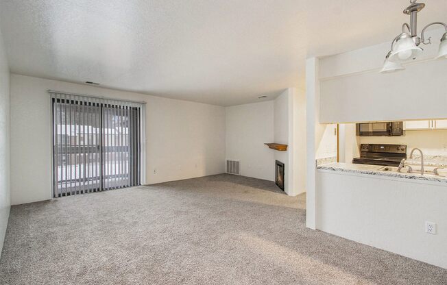 an empty living room with a window and a kitchen