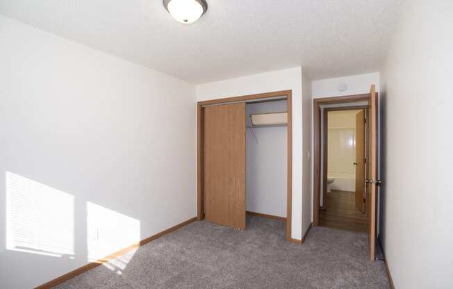 an empty living room with a door to a closet and a hallway to a bathroom. Fargo, ND Country Club Apartments