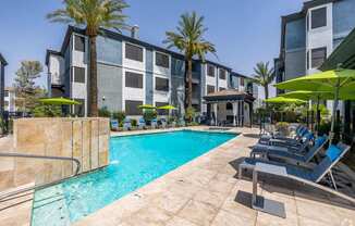 A pool surrounded by lounge chairs and umbrellas in front of a building.