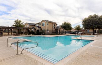 Swimming pool with tanning deck, green trees, and view of the clubhouse in the background