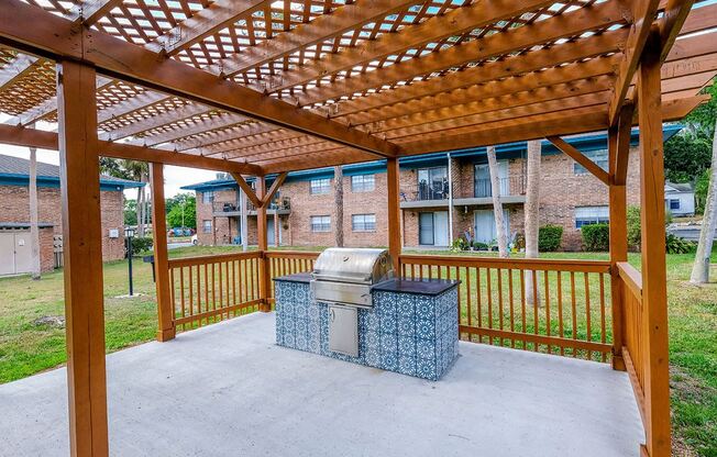 BBQ area at Watermarc Apartments in Lakeland, FL with stained wood trellis and large prep station with blue Spanish inspired tiles.