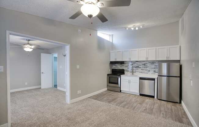 a living room with a ceiling fan and a kitchen with stainless steel appliances