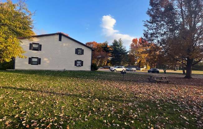 a house with a picnic table in a field with leaves on the ground