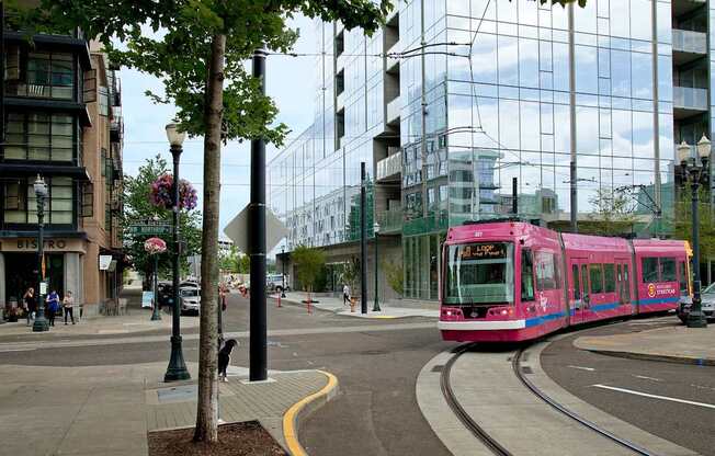 A pink tram is on the tracks in the middle of a city street.