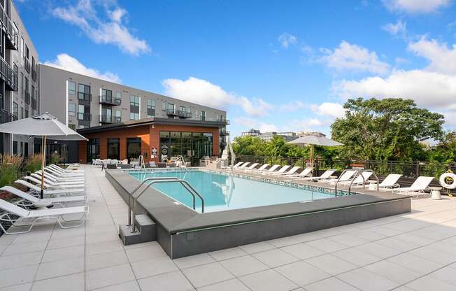 a swimming pool with chaise lounge chairs and umbrellas in front of a building