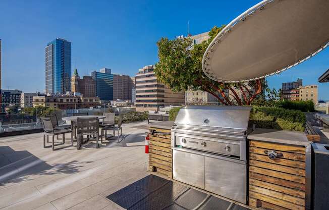 A stainless steel grill is on a patio with a city skyline in the background.