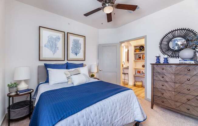 A bedroom with a blue bedspread and a ceiling fan.
