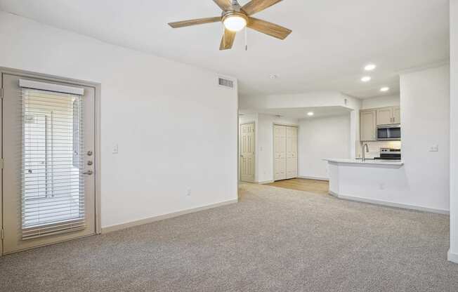 an empty living room with a ceiling fan and a kitchen