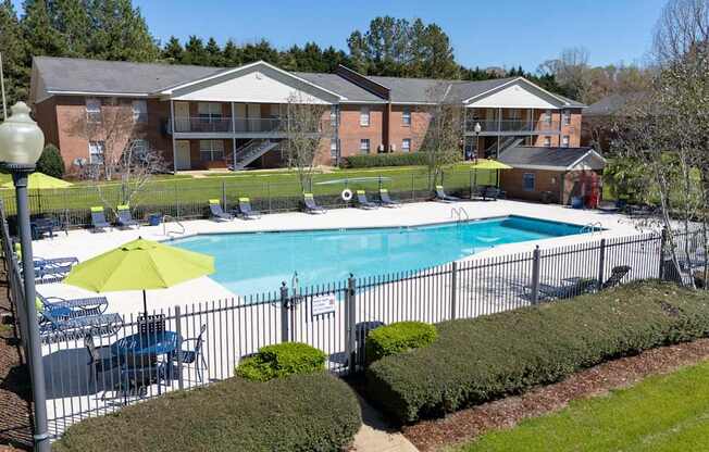 A pool surrounded by a fence and bushes with a building in the background.