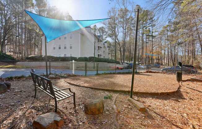 A park with a bench and a blue shade sail.