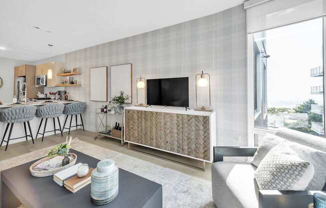 A modern living room with a grey sofa, a grey coffee table, a grey rug, a grey chair, a grey wall, a grey floor, a grey cabinet, a grey counter, a grey chair, a grey wall, a grey floor