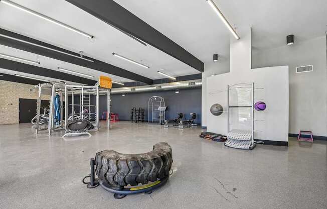 A gym with a variety of equipment including a tire flipper, a bench, and a rowing machine.