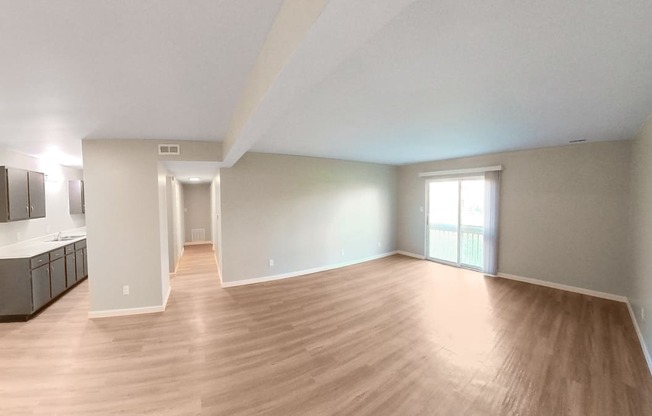 an empty living room with wood flooring and a kitchen